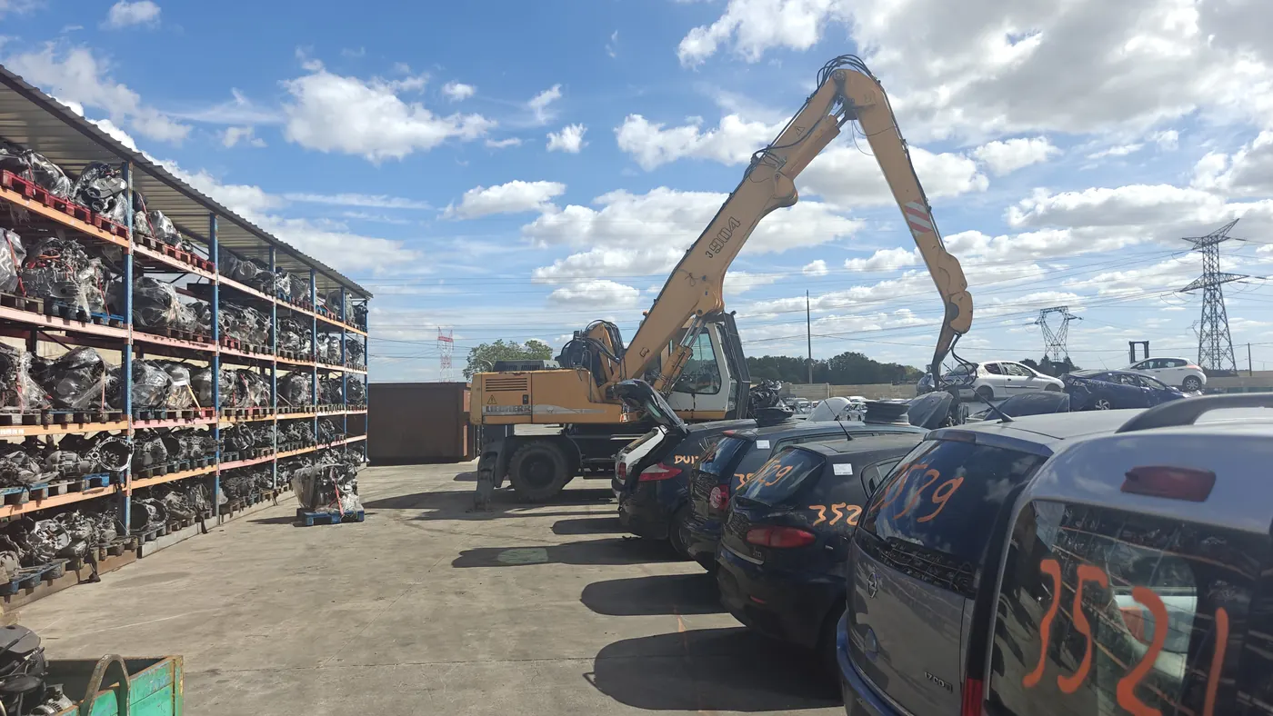 Cour de notre casse auto à Moret-Loing-et-Orvanne (77) : rayonnages de moteurs, pelle jaune bras levé, voitures numérotées
