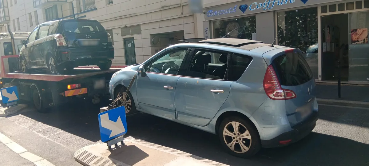 Corolla Verso abîmée arrimée au plateau, Scénic bleu au lève-roues, dans une rue de Clichy voisine de Levallois-Perret