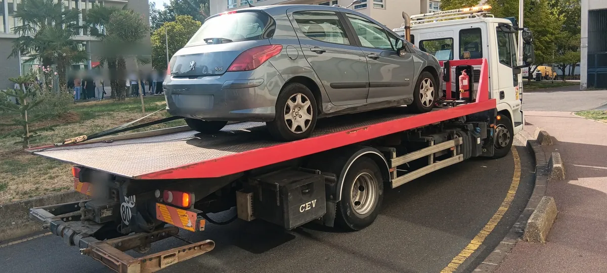 Peugeot 308 grise maintenue par des sangles sur un camion plateau blanc et rouge, entre résidences et bureaux de Créteil