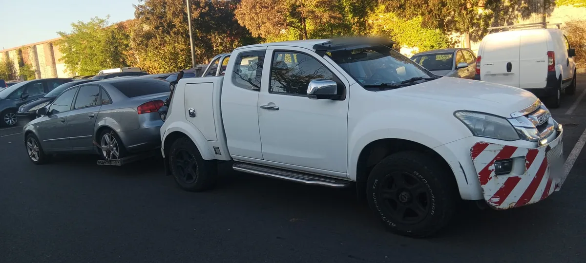 Berline Audi grise levée par l'arrière sur le lève-roues d'un pick-up blanc, sur un grand parking de Grigny au crépuscule